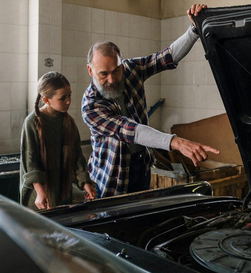 Mechanic man next to a car teaching a girl